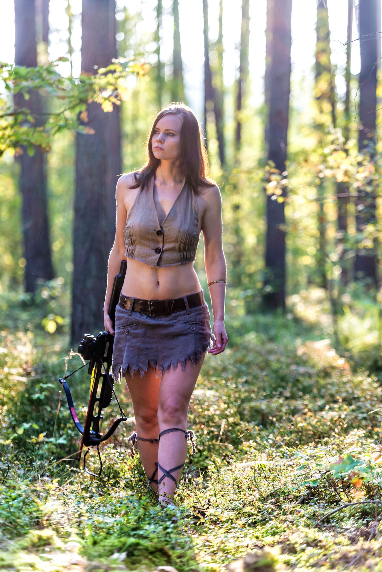 A girl with a arbalet goes hunting in the woods.