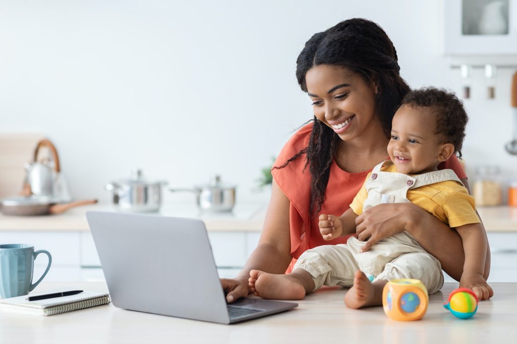 Black Mother Taking Care About Baby And Working On Laptop At Home