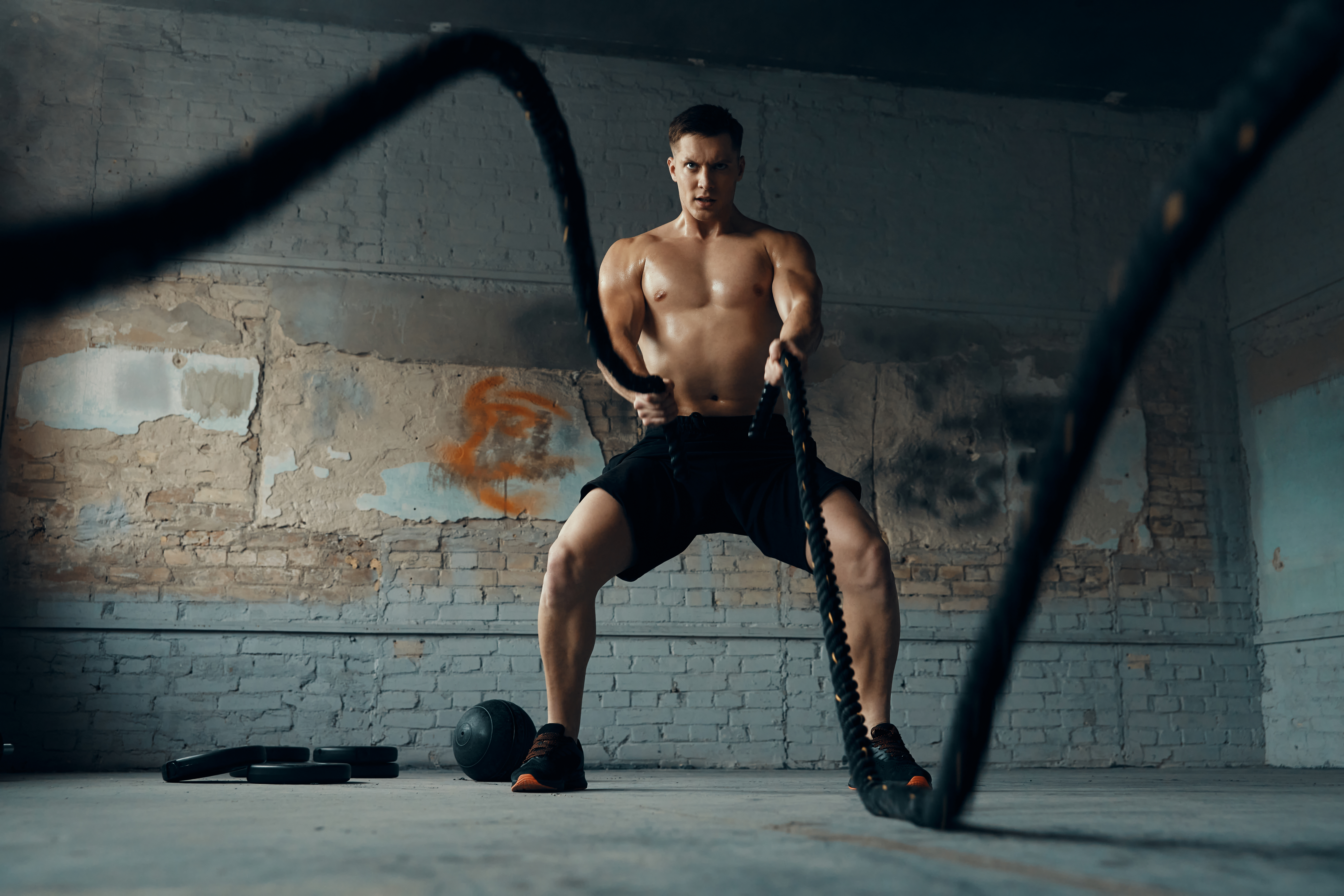 Confident young man exercising with battle rope in gym
