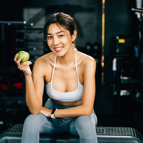 Asian woman holding a green apple in a fitness gym